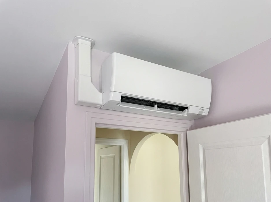 Unité intérieure de climatisation réversible murale, marque Mitsubishi Electric, modèle type MSZ, installée en hauteur au-dessus d'une porte intérieure