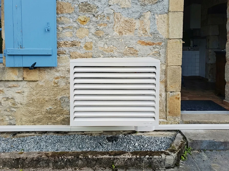 Unité extérieure de pompe à chaleur air/air installée sur platine murale, façade en pierre calcaire, volet bois peint en bleu