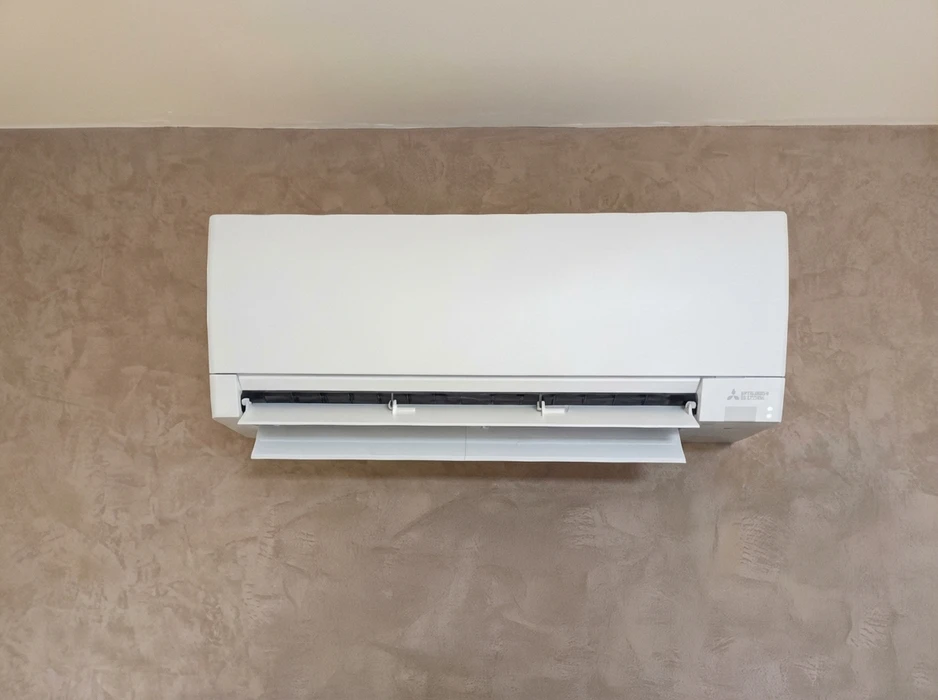 Unité intérieure de climatisation réversible murale, marque Mitsubishi Electric, modèle MSZ, installée en position haute sur un mur à enduit décoratif beige